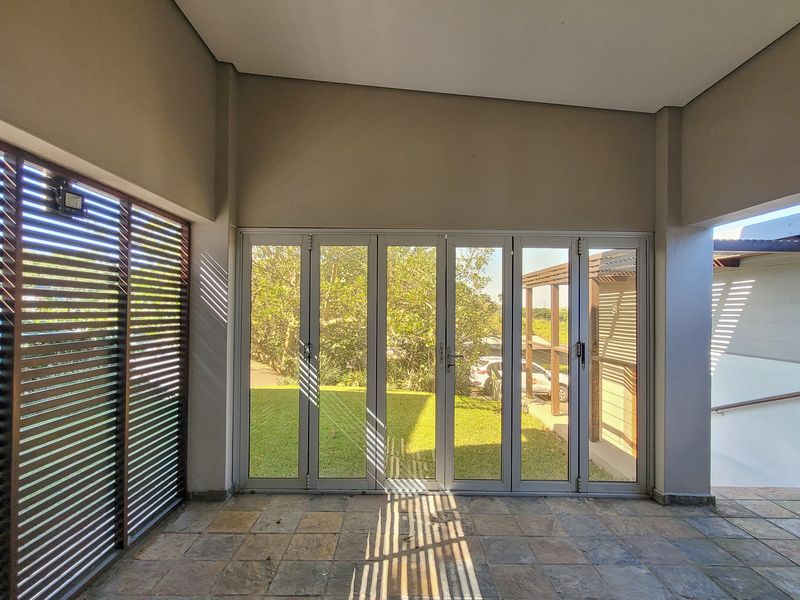 A covered patio area featuring stone tile flooring, timber louvre shutters, and large aluminium stacker doors opening onto the garden.