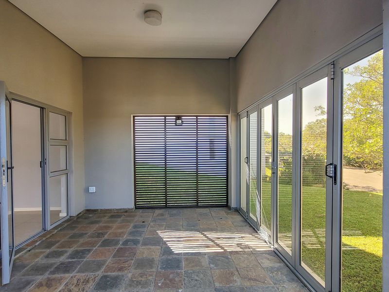 A covered patio area featuring durable tiled flooring, aluminium stacker doors providing garden access, and a slatted privacy screen.