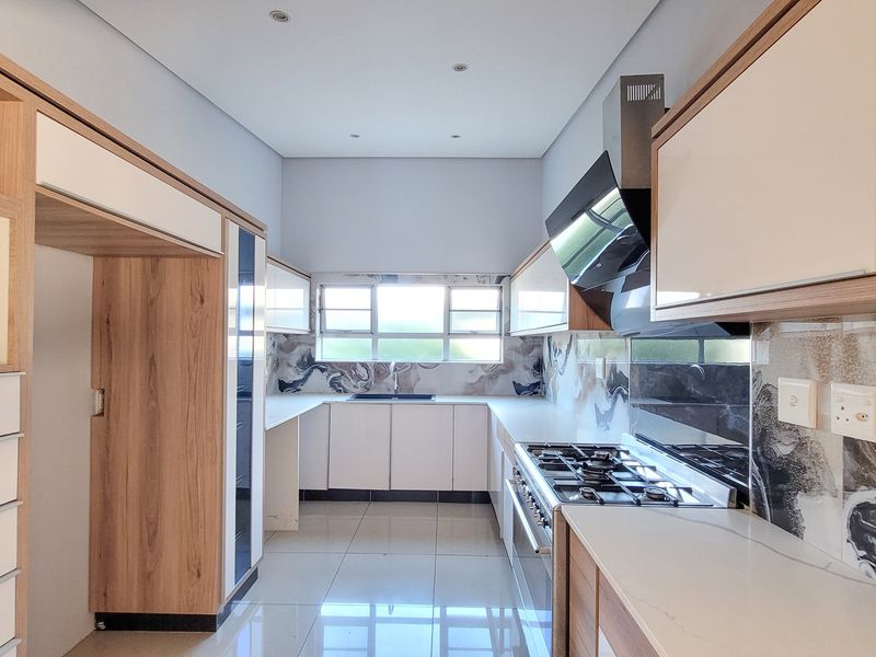 Modern kitchen featuring sleek wood-tone and white cabinetry, stone countertops, gas hob with extractor, and high-quality tiled flooring in a clean, contemporary layout.