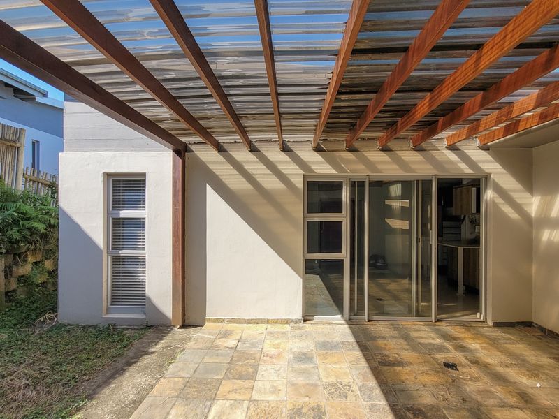 A covered patio area featuring a timber pergola with polycarbonate roofing, tiled flooring, and sliding glass doors leading into the home.