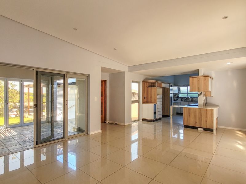 Spacious open-plan living area featuring large sliding glass doors, polished tile flooring, and a modern kitchen with built-in cabinetry and island.