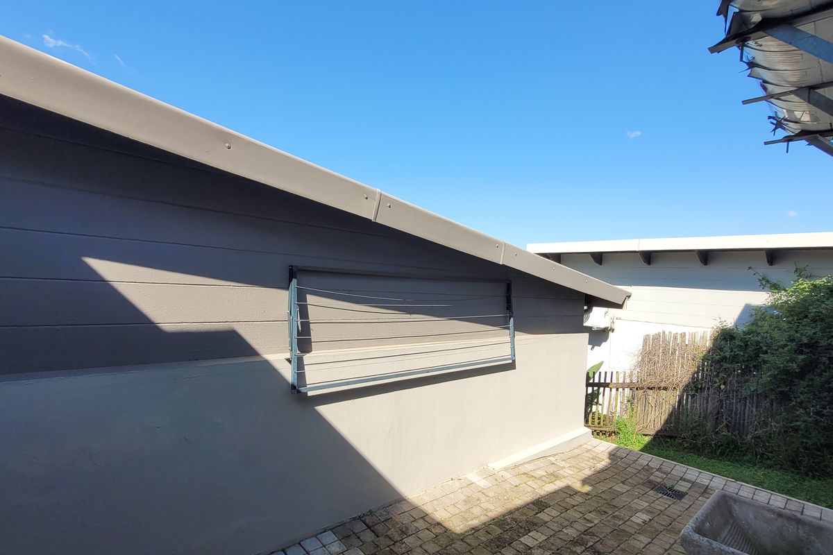 A rear exterior view showing a paved patio area, a wall-mounted clothesline, and a concrete wash trough against the side of the house.