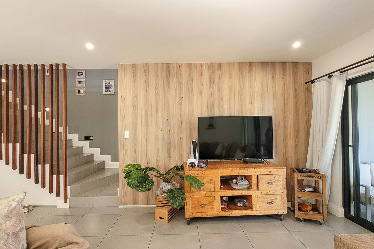 Modern living area featuring a wood-paneled feature wall, tiled flooring, and a contemporary staircase with timber slat balustrades leading to the upper level.