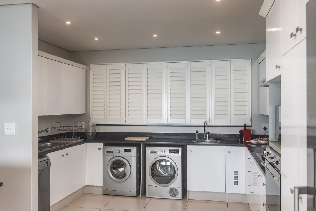 A modern, well-appointed kitchen featuring white cabinetry, dark stone countertops, integrated appliances, and plantation shutters over the window.