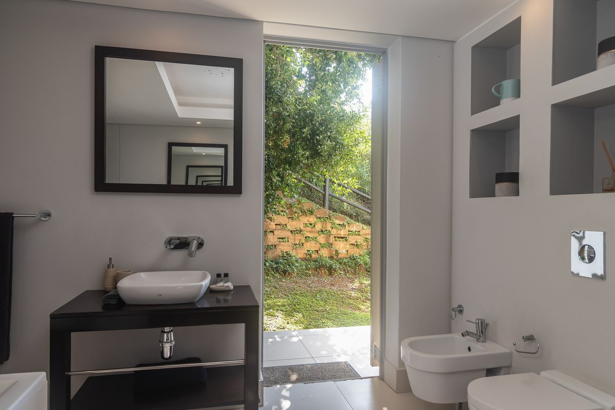 Modern bathroom featuring a vessel sink vanity, wall-mounted bidet and toilet, built-in shelving, and direct access to a private garden area.