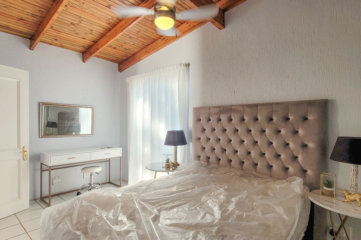 A bedroom featuring a vaulted timber ceiling, tiled flooring, and a neutral color palette, offering a cozy and functional living space.