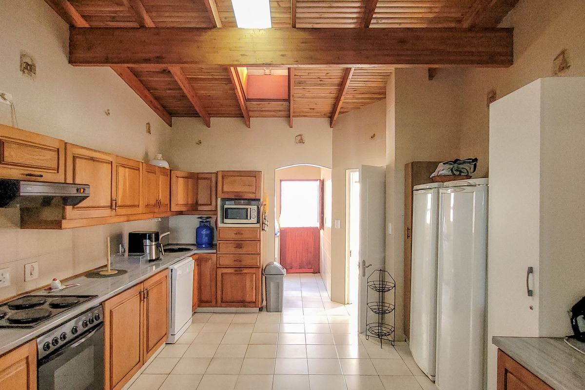A functional kitchen featuring timber cabinetry, built-in oven and hob, tiled flooring, and a vaulted timber-beamed ceiling with a skylight.