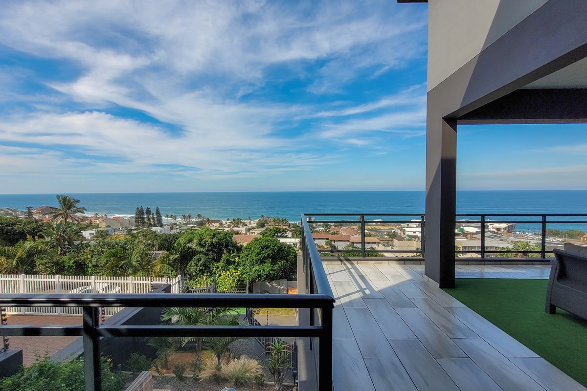 Spacious covered balcony featuring modern tiled flooring, artificial turf, and a glass balustrade, offering expansive panoramic ocean and coastal views.