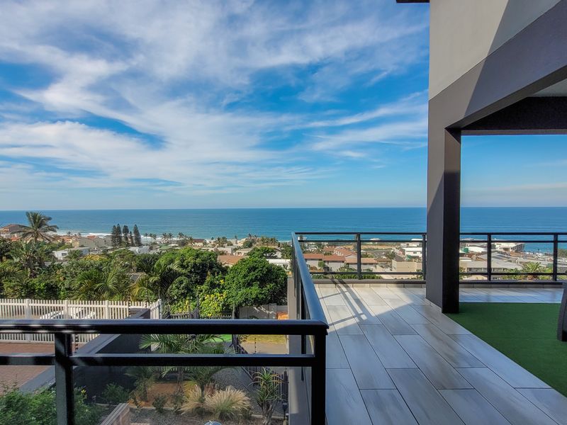 Spacious covered balcony featuring modern tiled flooring, artificial turf, and a glass balustrade, offering expansive panoramic ocean and coastal views.