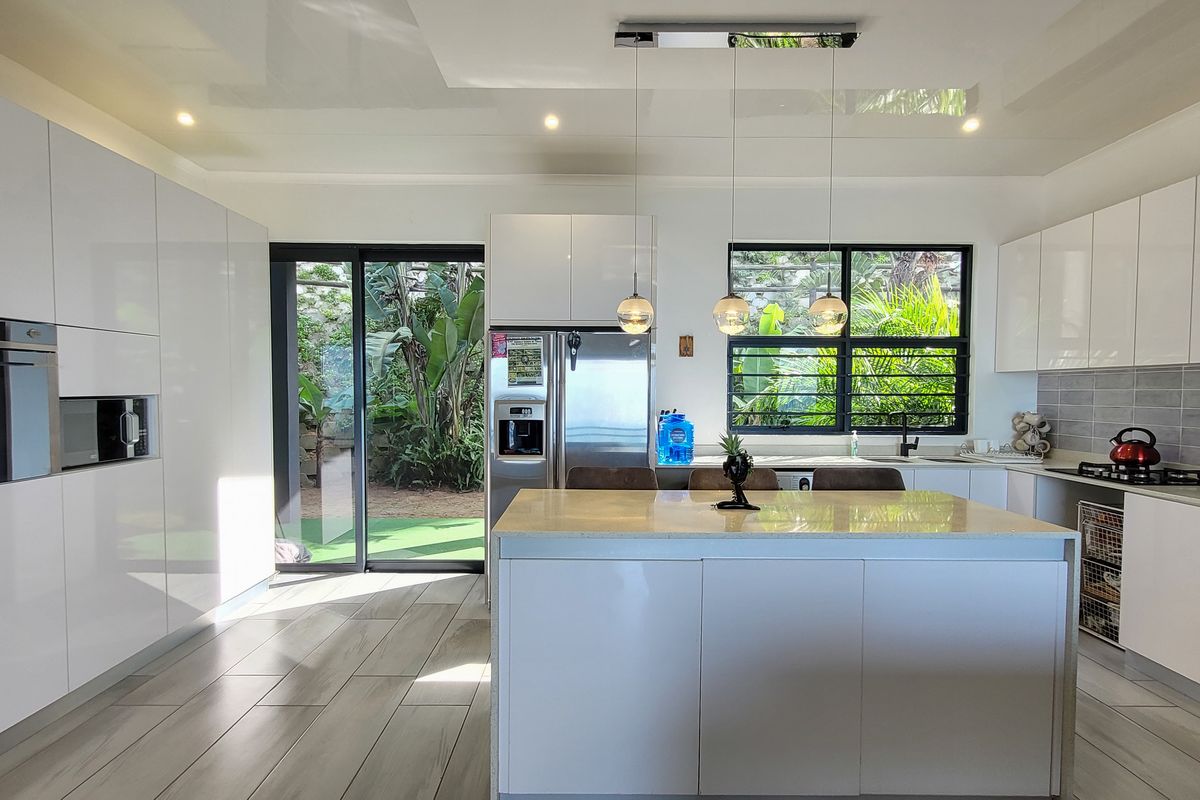 Modern kitchen featuring high-gloss cabinetry, a central island with stone countertops, built-in appliances, and direct access to the garden through sliding glass doors.