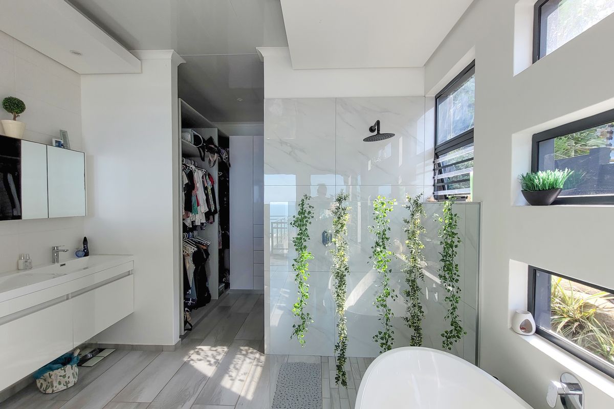 Modern bathroom featuring a wall-mounted vanity, freestanding bathtub, walk-in shower with rain head, and an integrated walk-in wardrobe area.