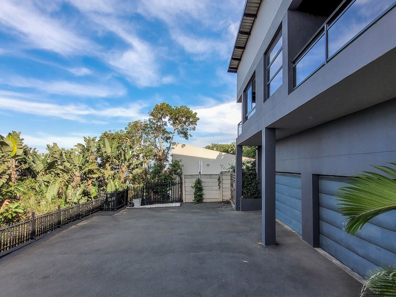 Modern multi-story residential property featuring a double garage, paved driveway, and an upper-level balcony with glass balustrades.