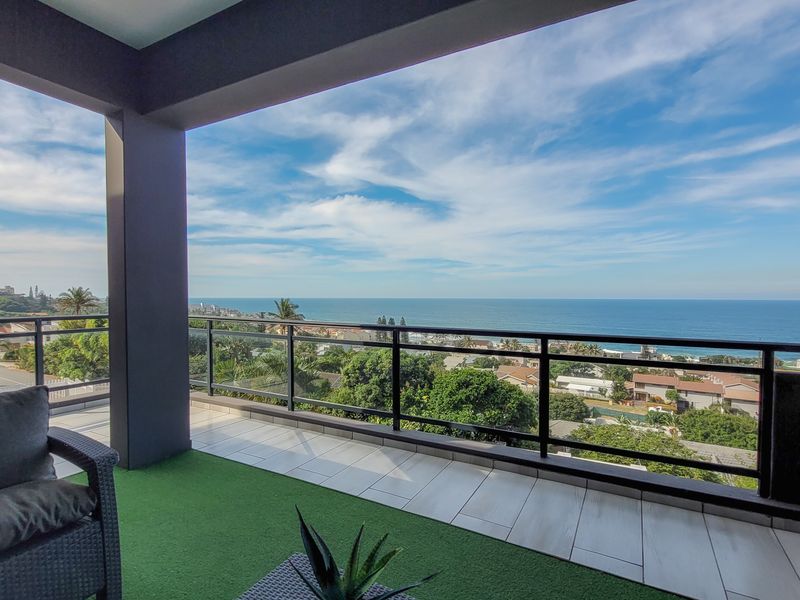 Spacious covered balcony featuring modern tiled flooring, a sleek glass balustrade, and expansive panoramic ocean views.