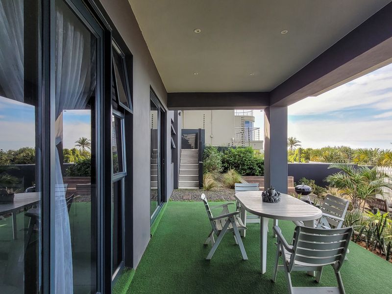 A covered outdoor patio featuring artificial turf flooring, recessed lighting, and large sliding glass doors providing seamless access to the interior living space.
