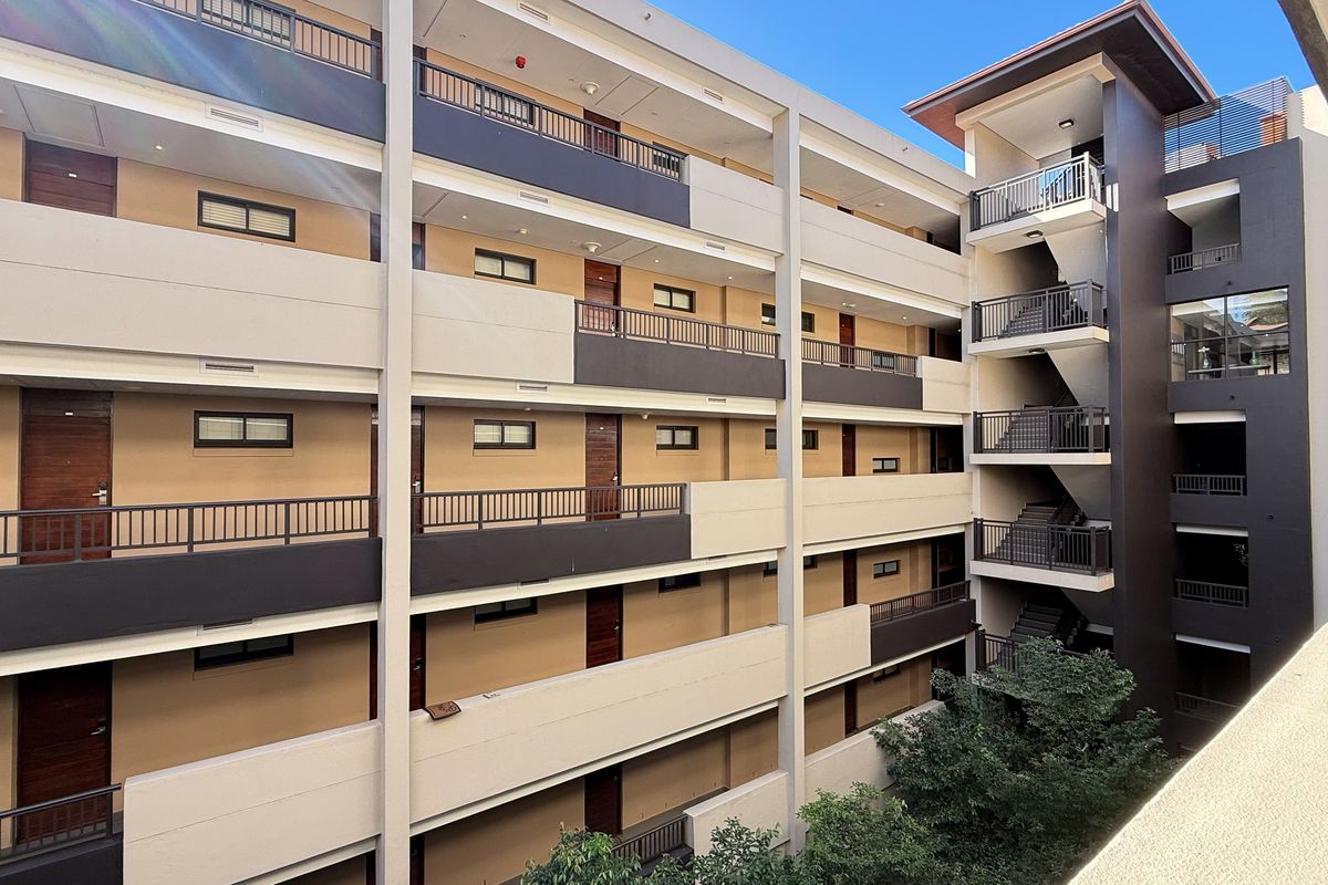 Exterior view of a multi-story apartment building featuring open-air walkways, metal railings, and a central stairwell structure.