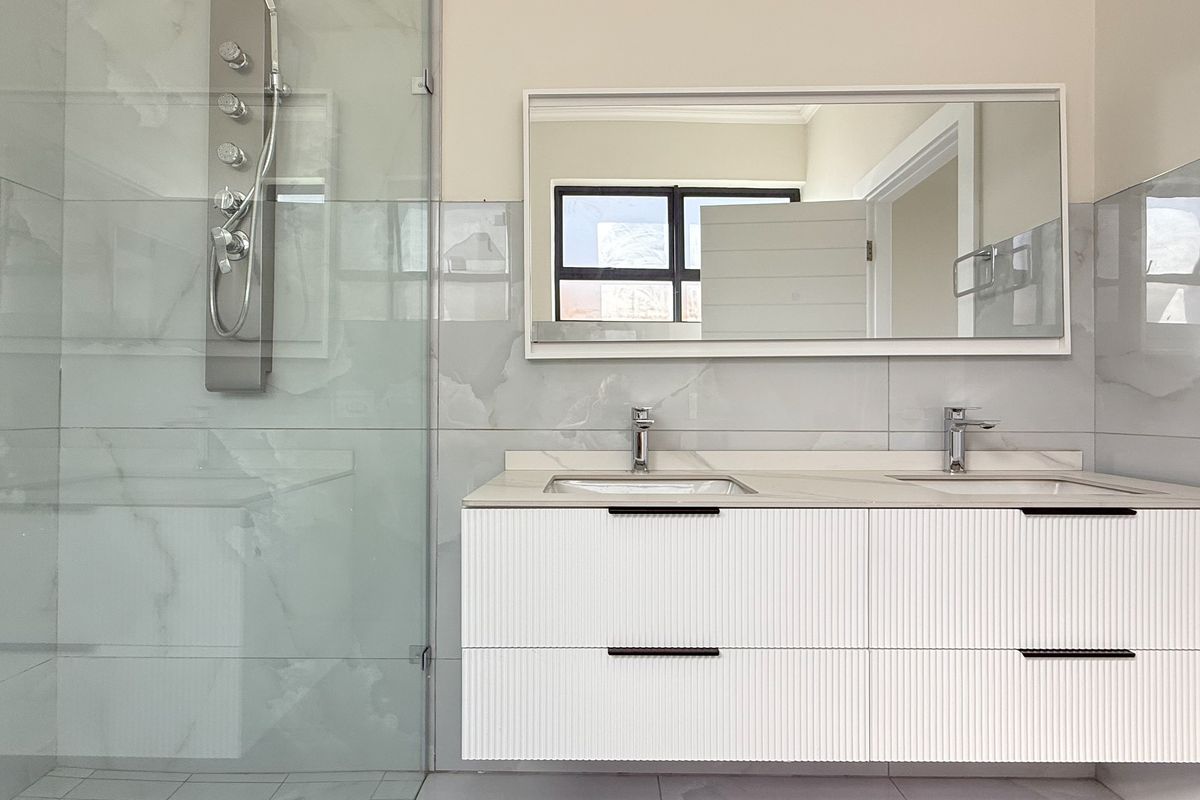 Modern bathroom featuring a double vanity with wall-mounted cabinetry, a large mirror, and a glass-enclosed shower with a contemporary shower panel.