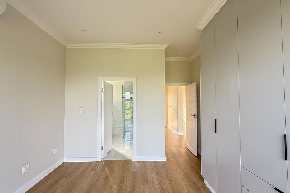 A bright, modern bedroom featuring light laminate flooring, extensive built-in cupboards, crown molding, and an en-suite bathroom.