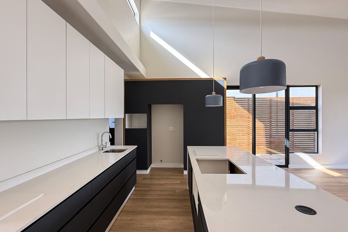 Modern kitchen featuring a large island, quartz countertops, sleek two-tone cabinetry, and a vaulted ceiling with a skylight, creating a bright and spacious atmosphere.