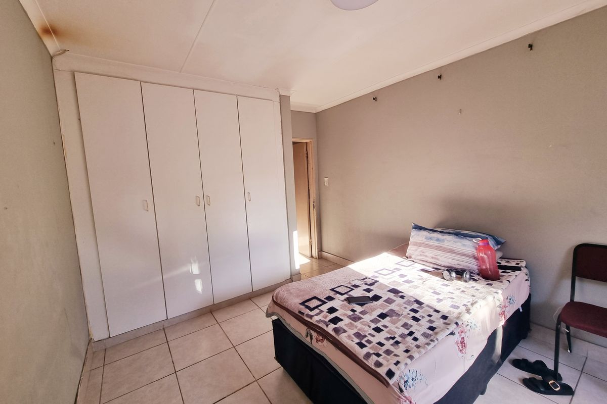 A bedroom featuring built-in cupboards and tiled flooring, showing signs of wear including ceiling water damage.