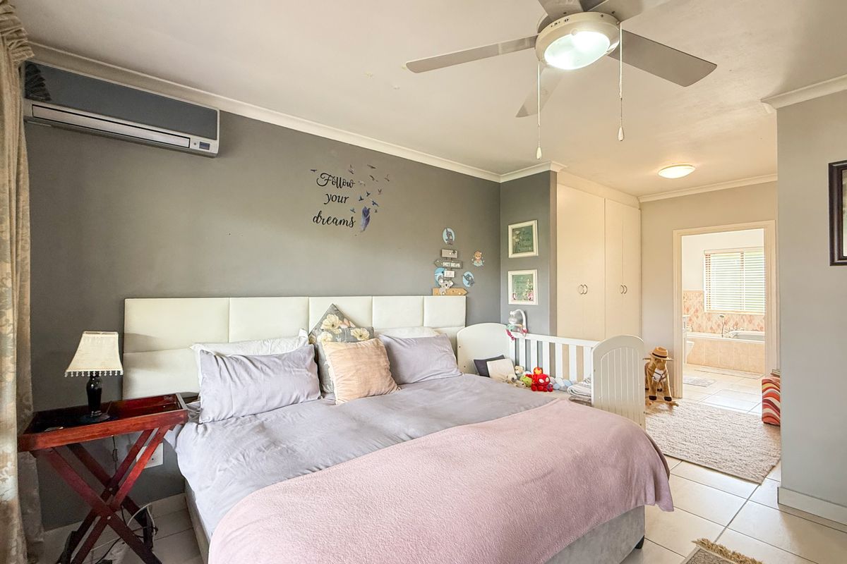 Spacious bedroom featuring built-in cupboards, a ceiling fan, and an integrated air conditioning unit, with direct access to an en-suite bathroom.