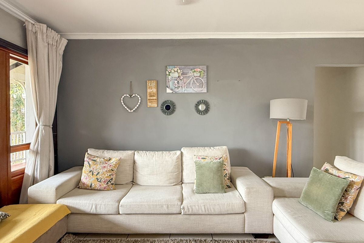 A well-maintained living room featuring neutral grey walls, tiled flooring, and a large window with curtains providing natural light.