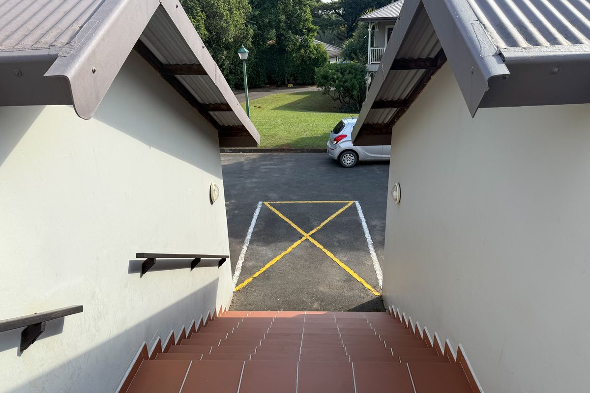 An outdoor staircase with tiled steps and metal handrails leading down to a paved parking area with marked bays.