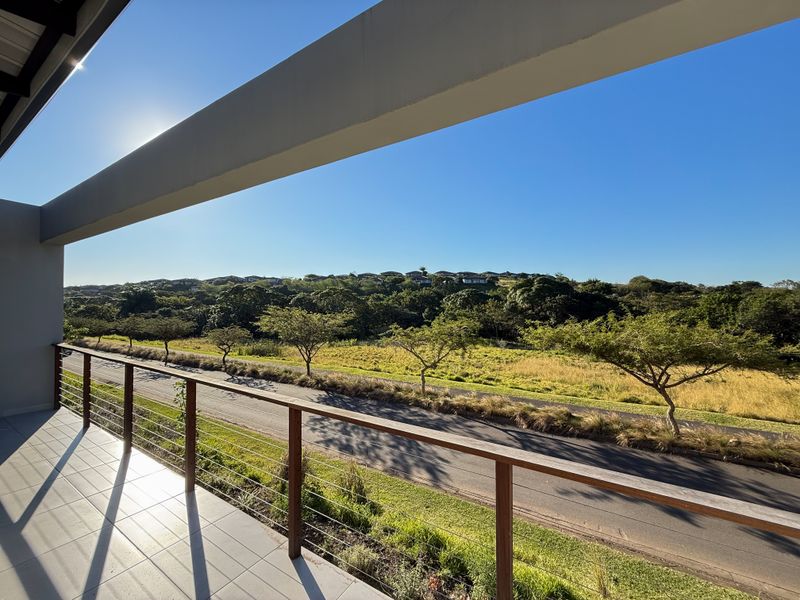 A spacious covered balcony featuring a modern timber and wire balustrade, offering expansive views over the surrounding landscape and neighborhood.