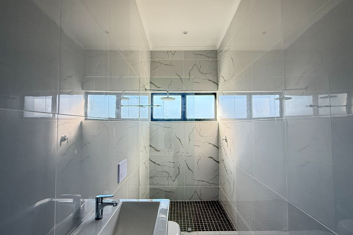Modern bathroom featuring floor-to-ceiling marble-look wall tiles, a walk-in shower with mosaic floor tiling, and a sleek wall-mounted basin.