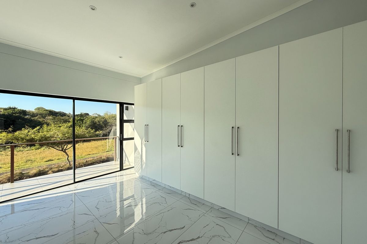 A bright, modern bedroom featuring floor-to-ceiling built-in cupboards, polished marble-look floor tiles, and large sliding glass doors opening to an outdoor balcony.