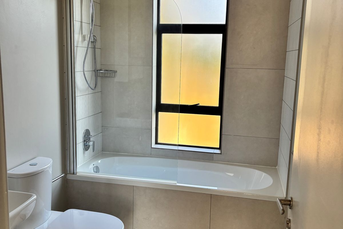 Modern bathroom featuring a built-in bathtub with a glass shower screen, shower mixer, and a contemporary toilet.