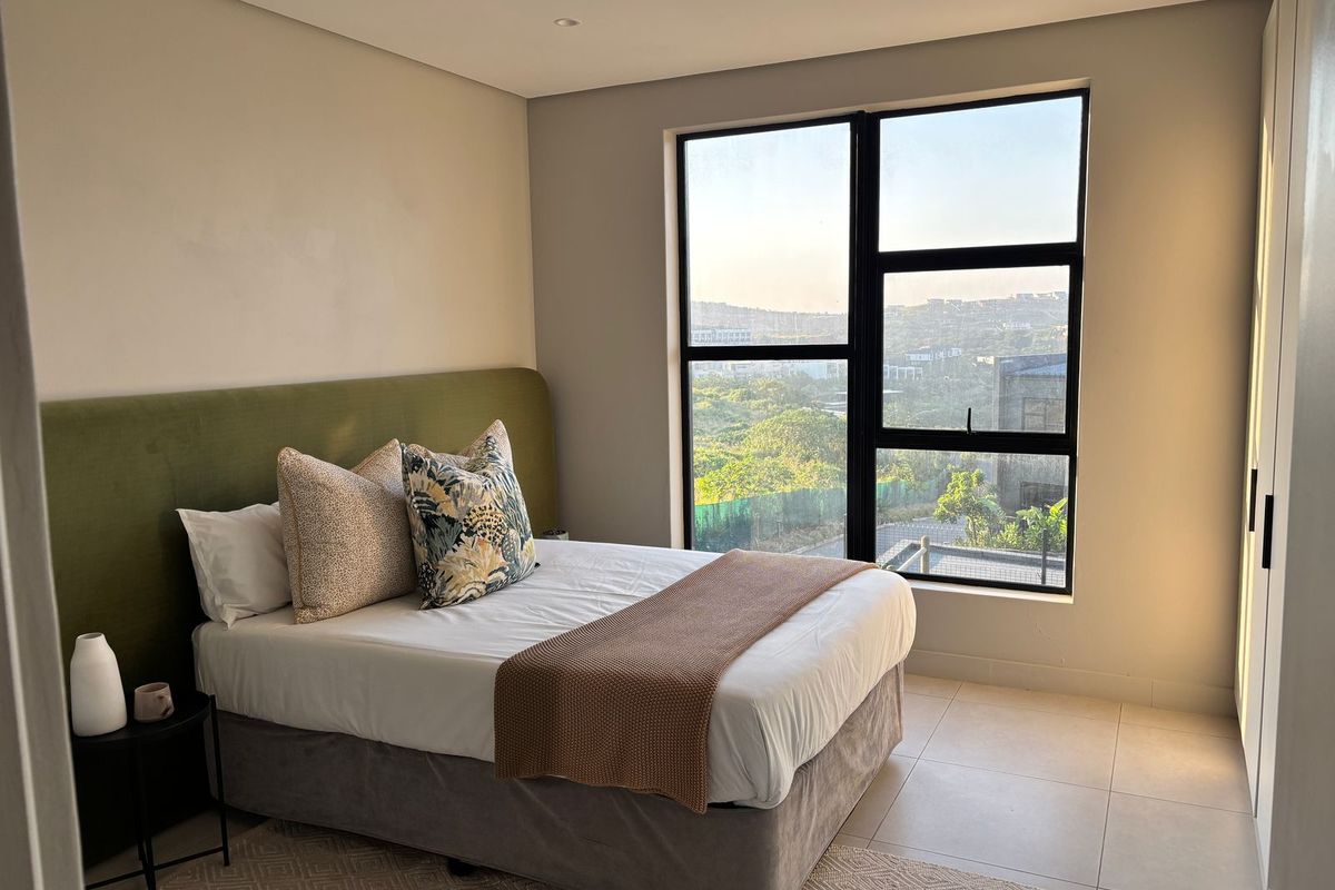 A bright bedroom featuring large windows with scenic views, neutral tiled flooring, and built-in cabinetry.