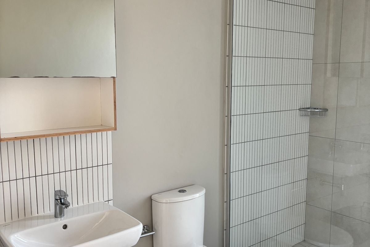 Modern bathroom featuring a wall-mounted basin, a sleek toilet, and a walk-in shower with contemporary vertical tile detailing.