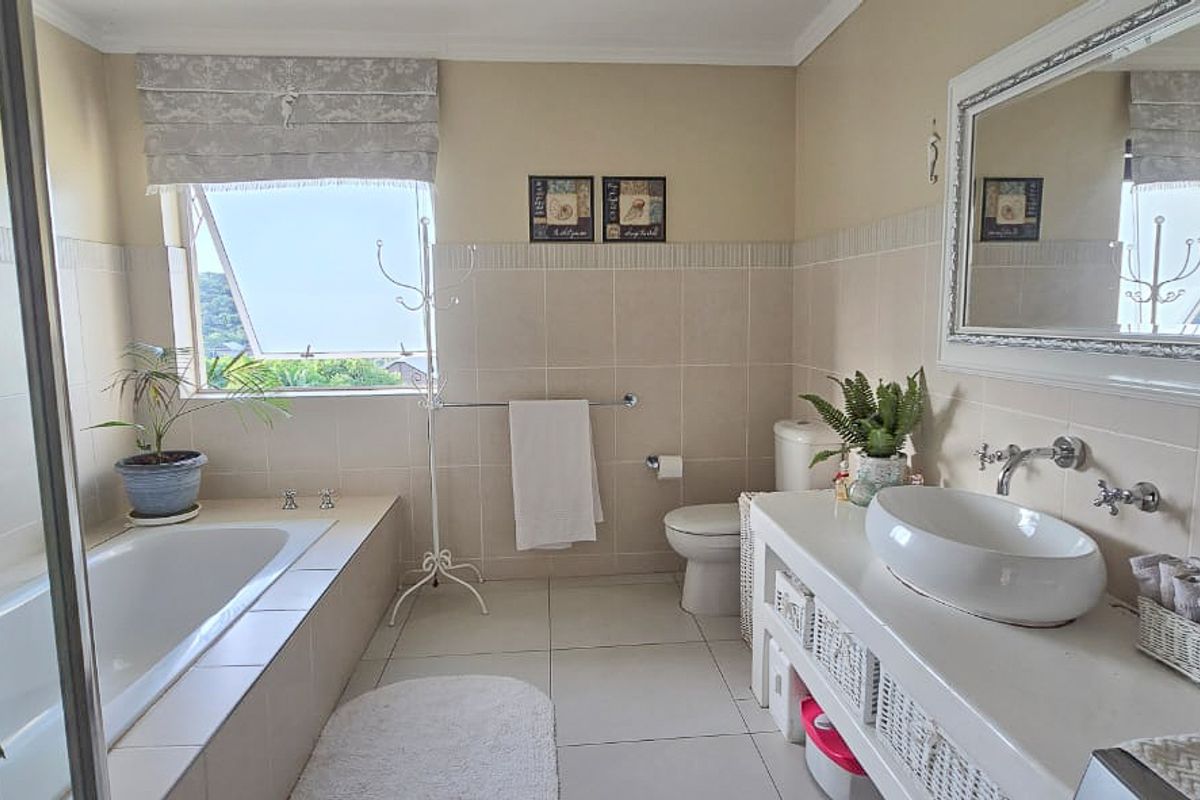 A well-lit bathroom featuring a built-in bathtub, a vessel sink vanity, a toilet, and neutral wall tiling.