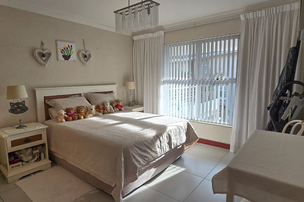 A well-lit bedroom featuring tiled flooring, vertical blinds, and a ceiling-mounted light fixture.