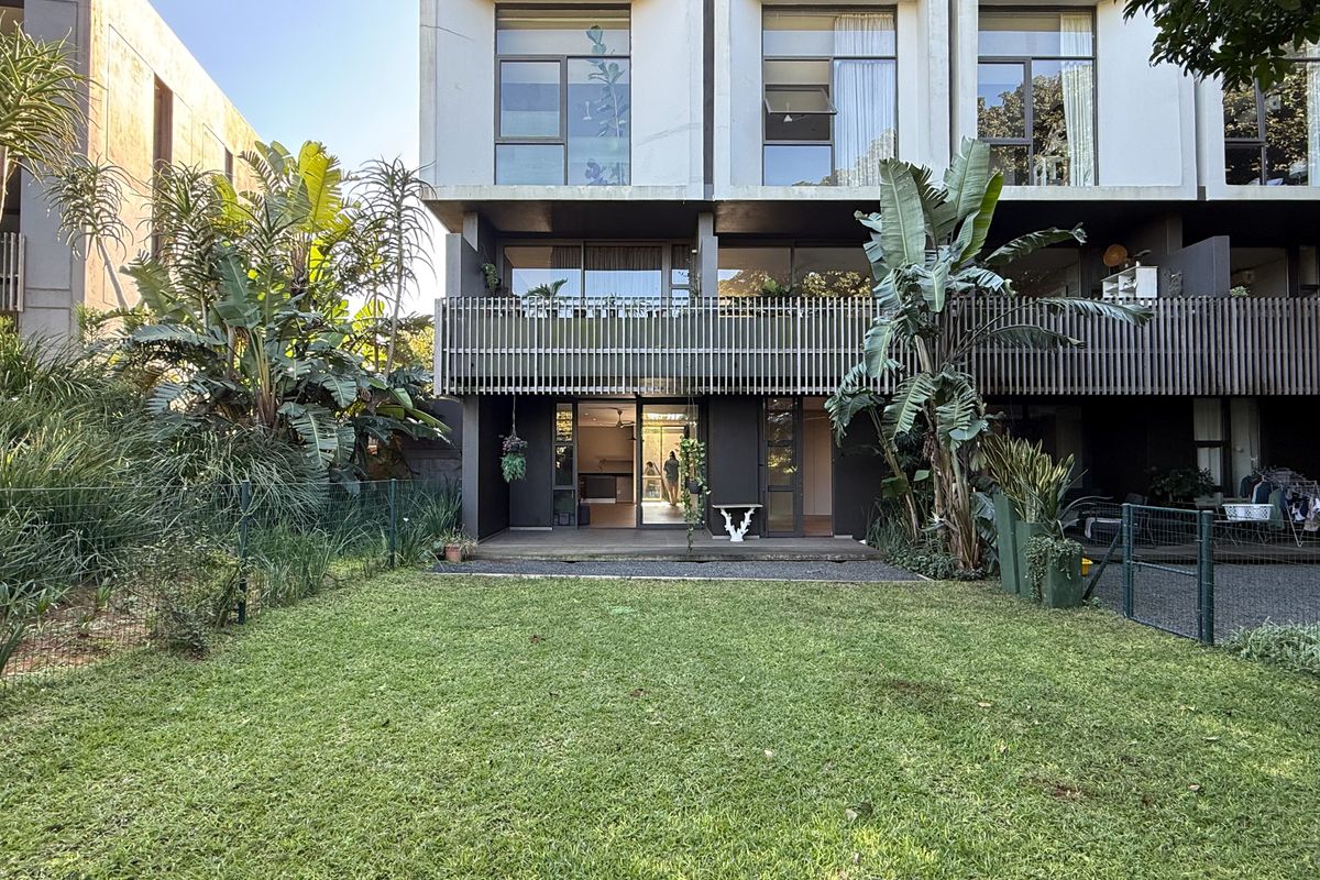 Rear view of a modern apartment building featuring a private garden, timber decking, and a balcony with slatted timber screening.
