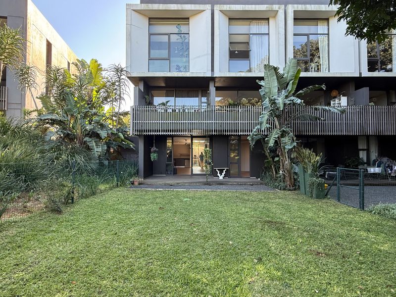 Rear view of a modern apartment building featuring a private garden, timber decking, and a balcony with slatted timber screening.