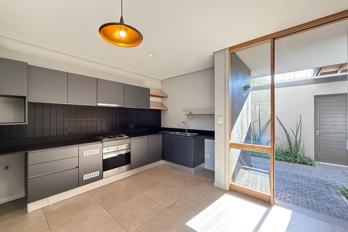Modern kitchen featuring sleek dark cabinetry, integrated gas hob and oven, tiled flooring, and direct access to a private paved courtyard.