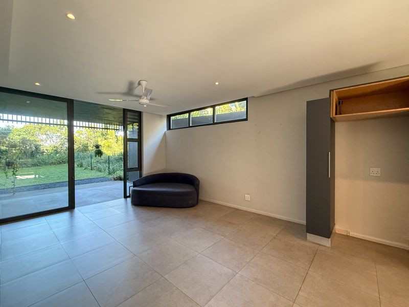 Spacious open-plan living area featuring large sliding glass doors, tiled flooring, recessed lighting, and built-in cabinetry with direct access to the garden.