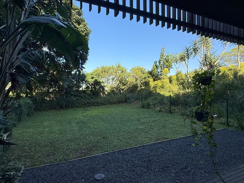 A covered patio area featuring a timber pergola overlooking a private garden with a well-maintained lawn and gravel border.