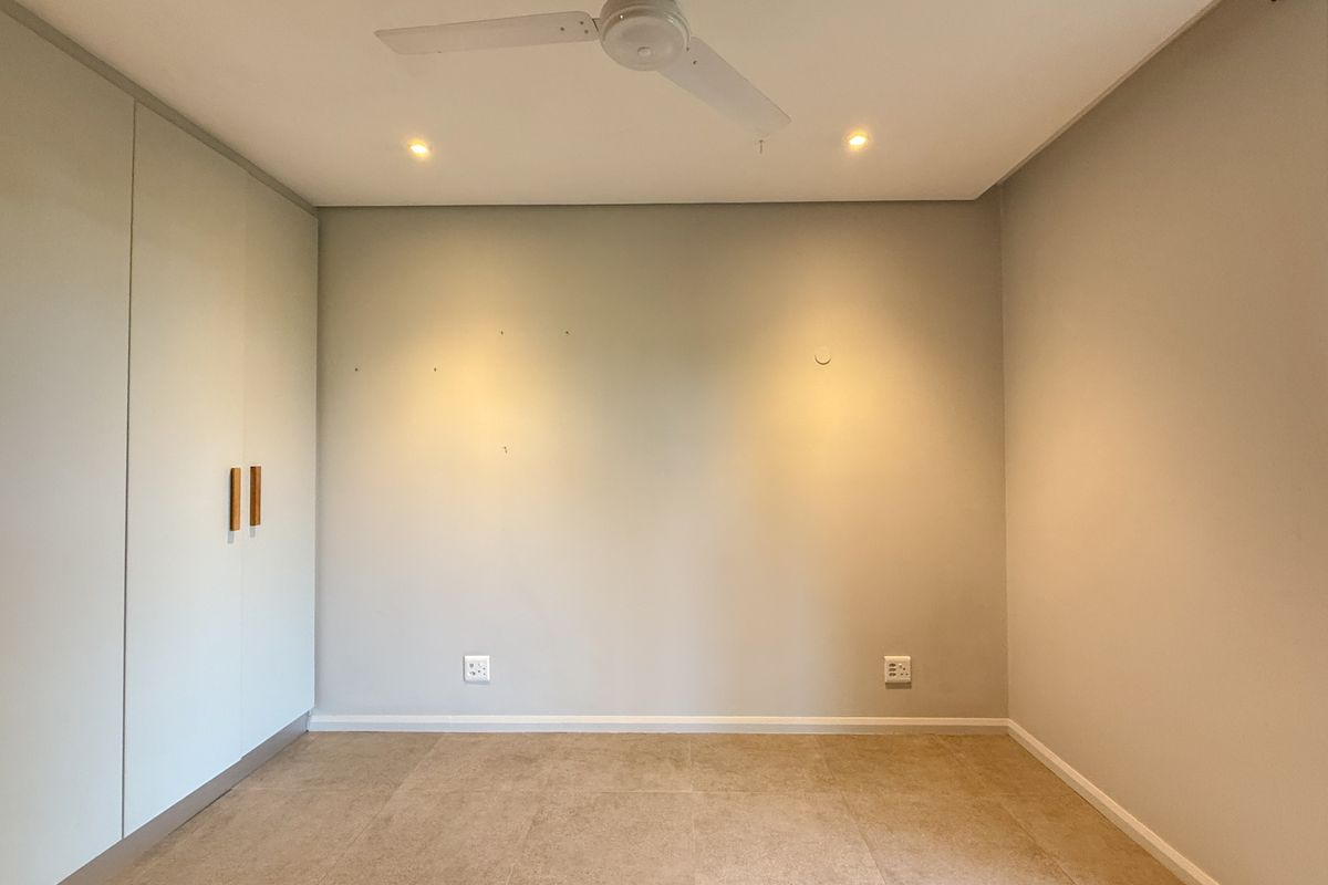 A clean, empty bedroom featuring neutral tiled flooring, built-in cupboards, a ceiling fan, and recessed lighting, ready for personalization.