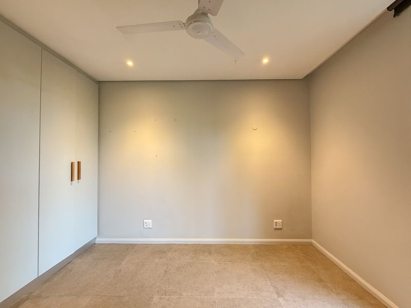 A clean, empty bedroom featuring neutral tiled flooring, built-in cupboards, a ceiling fan, and recessed lighting, ready for personalization.
