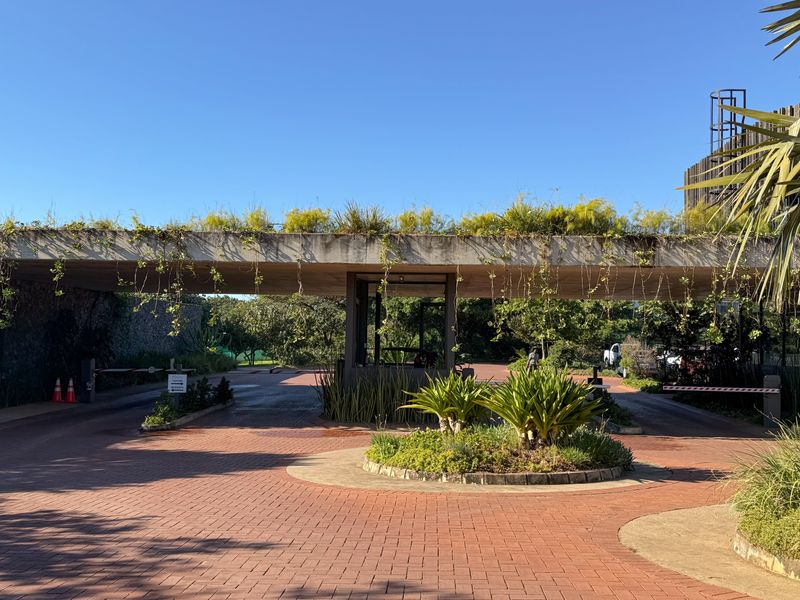 The property entrance features a modern security gatehouse with a concrete canopy, paved driveway, and landscaped traffic island.