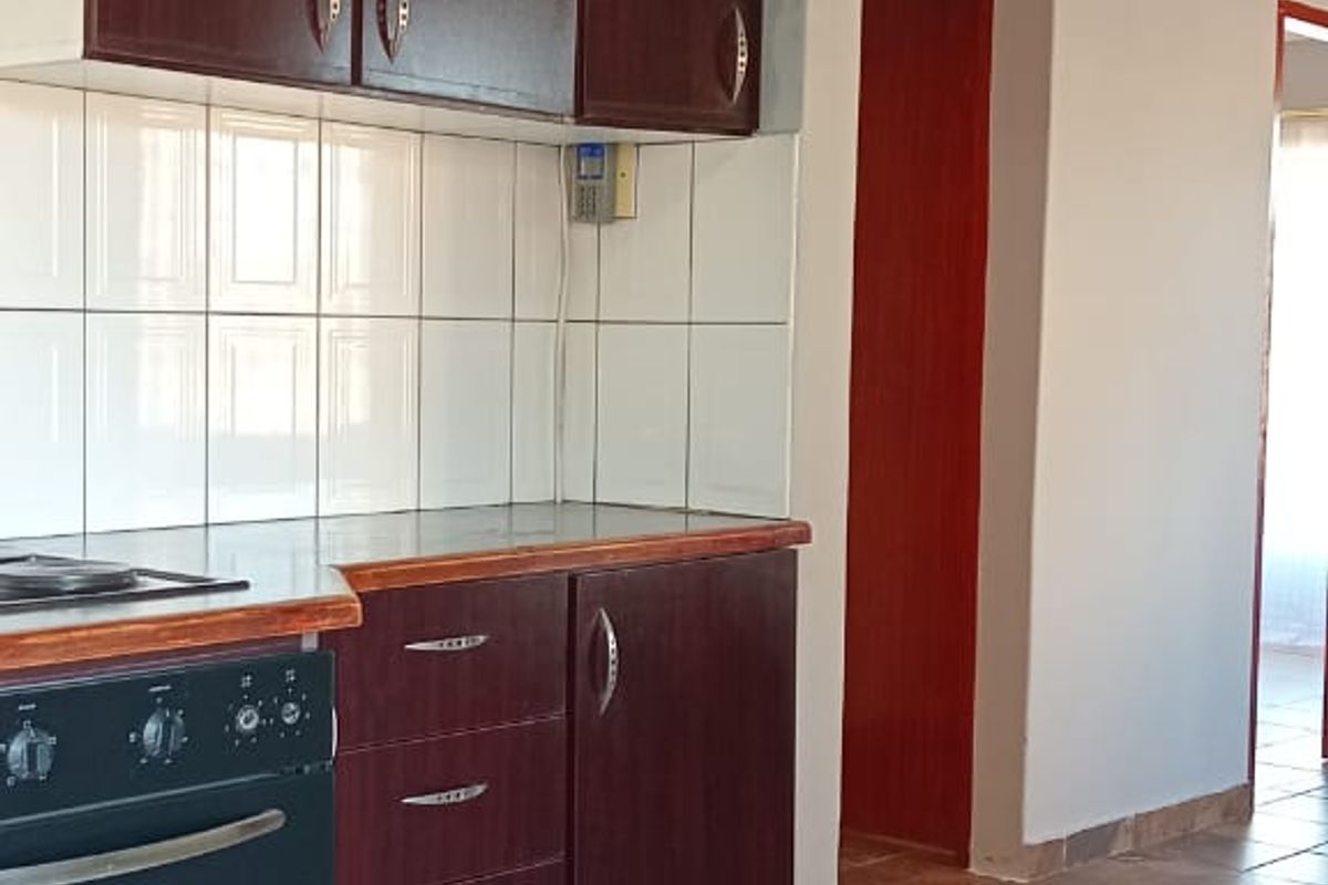 A functional kitchen featuring dark wood-toned cabinetry, a built-in oven, and tiled flooring, leading into an adjacent hallway.