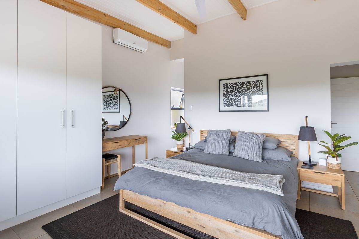 A bright and modern bedroom featuring exposed timber ceiling beams, built-in floor-to-ceiling wardrobes, and a wall-mounted air conditioning unit.