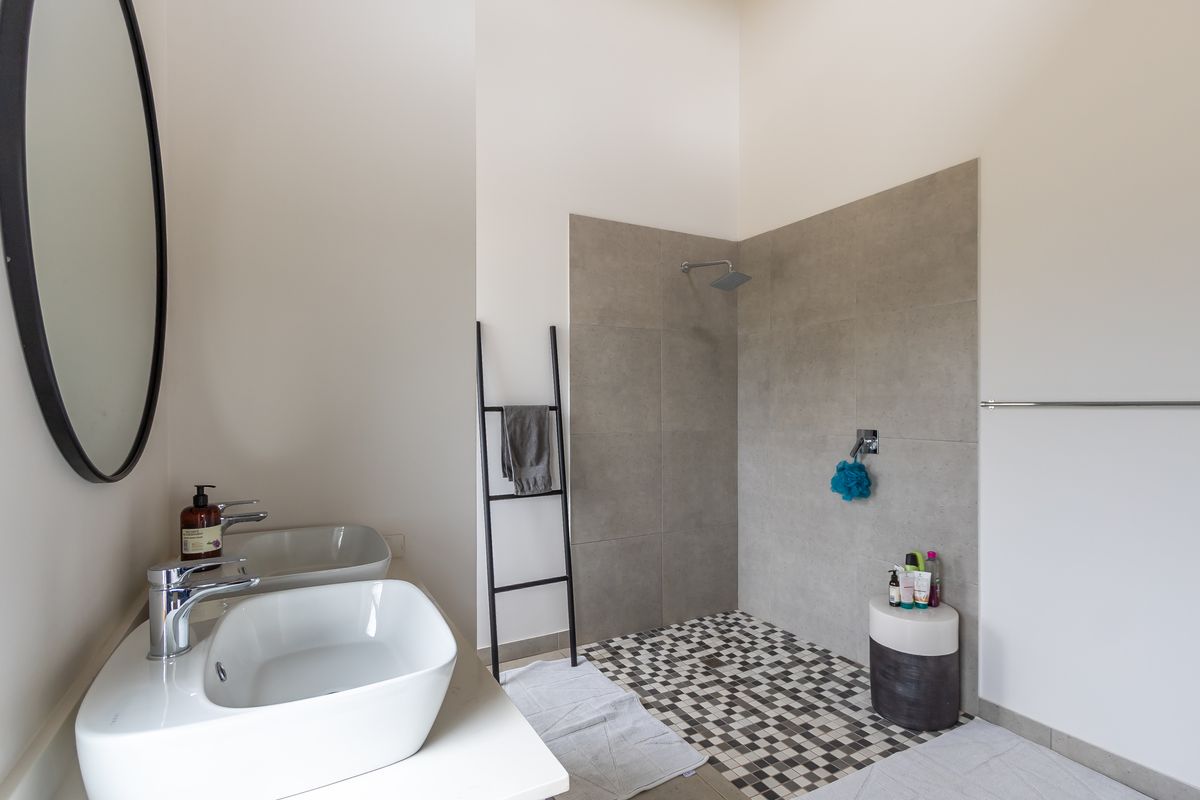 Modern bathroom featuring a walk-in shower with grey tiled walls, mosaic floor tiling, and a double vanity with vessel sinks.