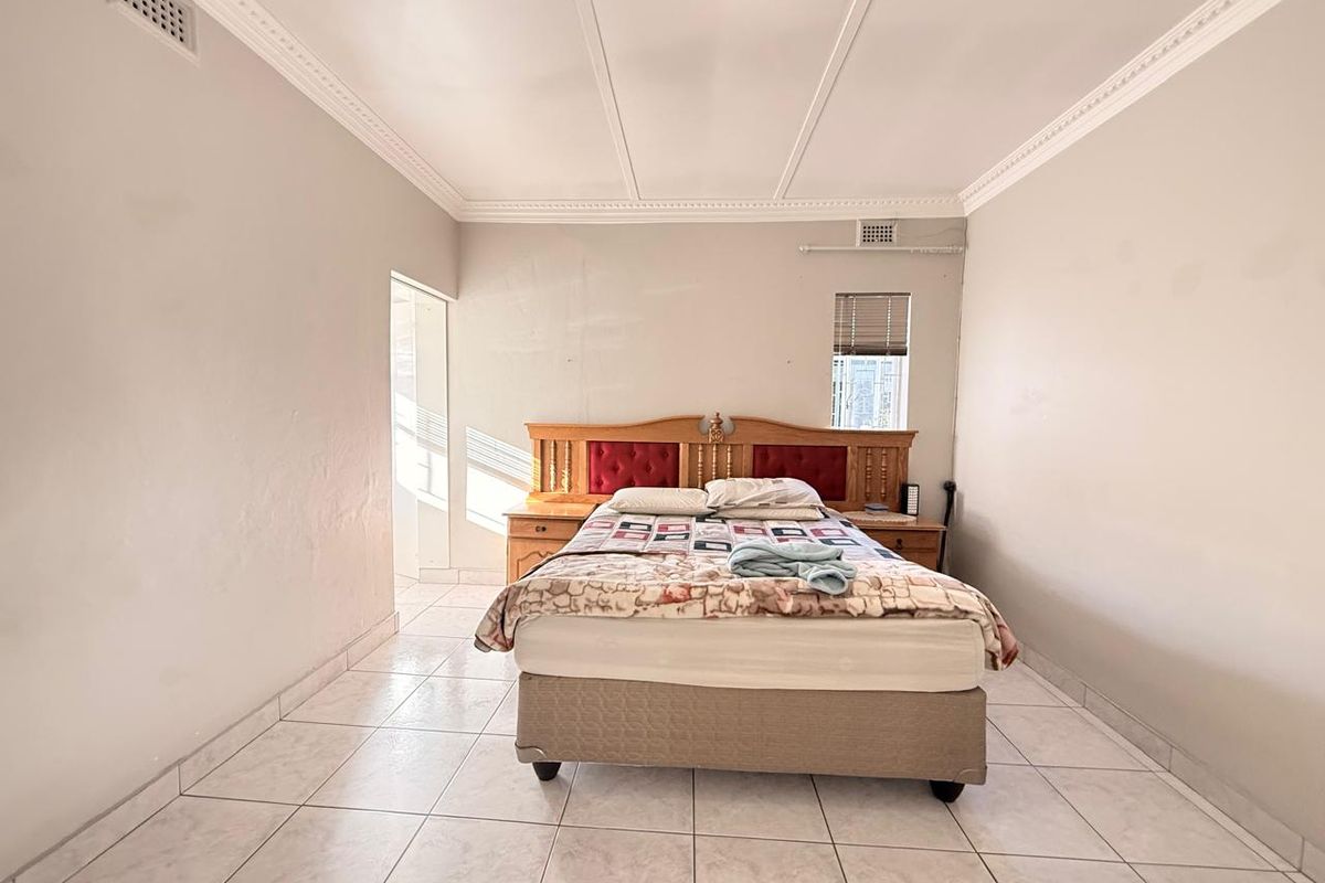 A spacious bedroom featuring tiled flooring, decorative ceiling cornices, and built-in ventilation vents.