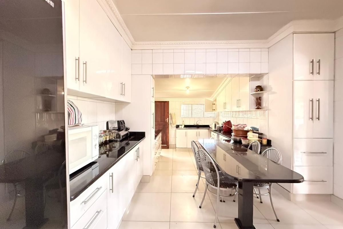 A spacious kitchen featuring white cabinetry, black granite countertops, tiled flooring, and an integrated breakfast bar area.