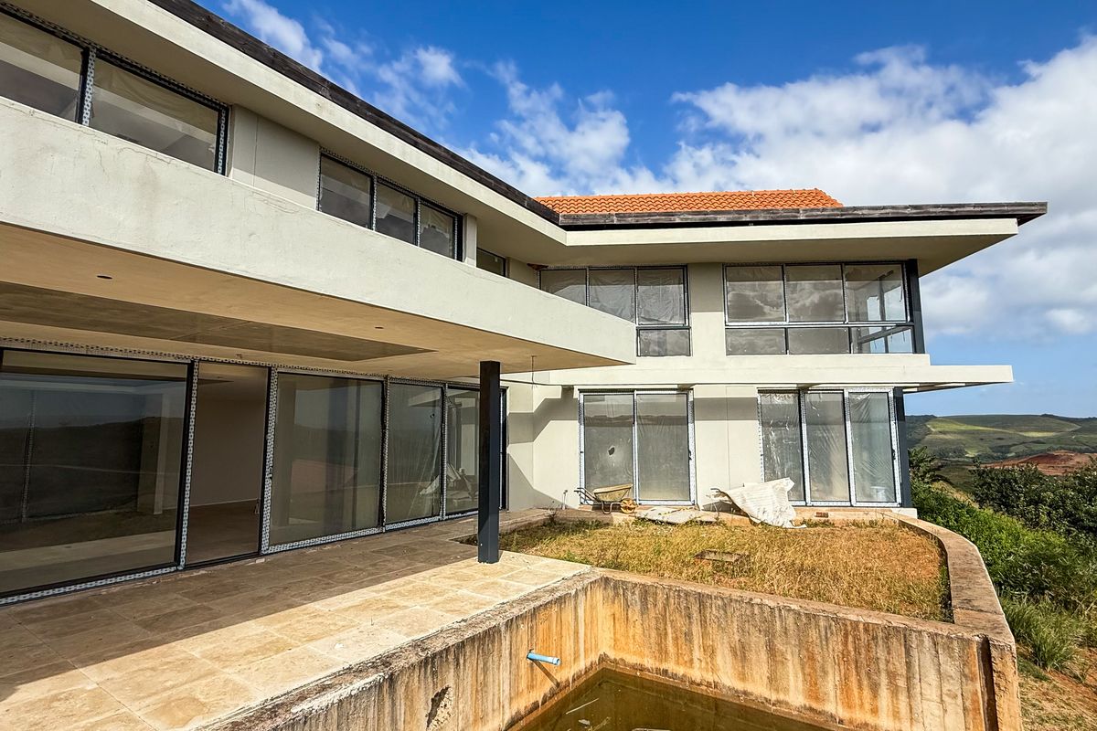 Rear view of a multi-level property featuring a large patio, swimming pool, and expansive glass sliding doors overlooking a scenic landscape.
