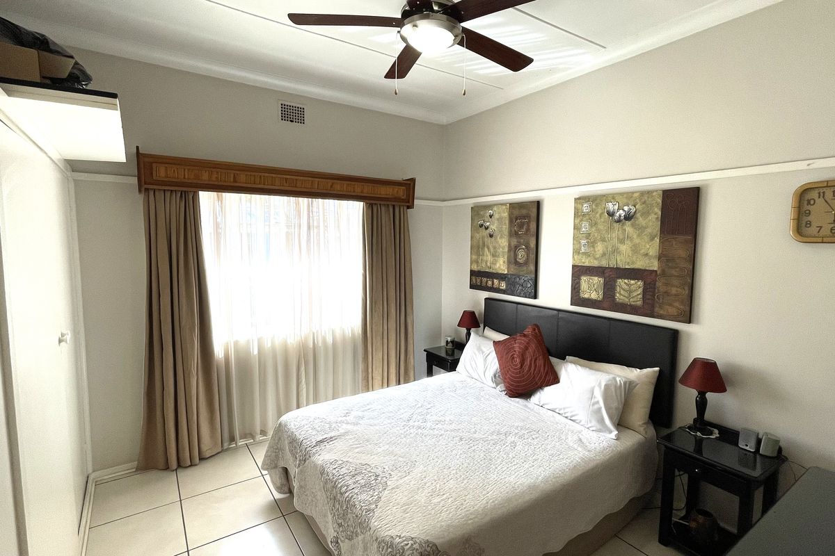 A well-maintained bedroom featuring tiled flooring, a ceiling fan, and built-in wardrobe storage.