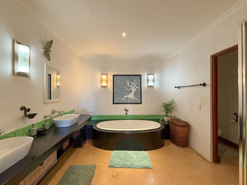 Spacious bathroom featuring a built-in oval soaking tub, dual vessel sinks on a dark vanity, and decorative wall sconces.